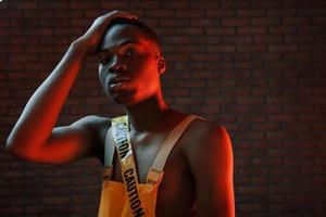 ruban de mise en garde jaune et uniforme. éclairage néon futuriste. jeune homme afro-américain dans le studio photo
