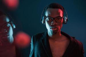 profiter de l'écoute de la musique dans les écouteurs. dans des verres. éclairage néon futuriste. jeune homme afro-américain dans le studio photo