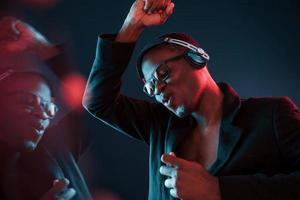 profiter de l'écoute de la musique dans les écouteurs. dans des verres. éclairage néon futuriste. jeune homme afro-américain dans le studio photo