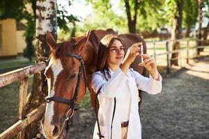 regarde la seringue. vétérinaire femelle examinant le cheval à l'extérieur à la ferme pendant la journée photo