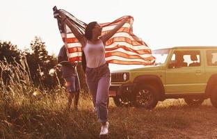 fille court en avant. les amis passent un bon week-end à l'extérieur près de leur voiture verte avec le drapeau américain photo