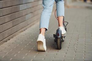 vue rapprochée d'une fille en vêtements décontractés qui fait du scooter électrique à l'extérieur pendant la journée ensoleillée photo