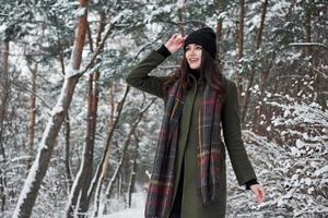 se demandant où aller ensuite. joyeuse jeune fille dans des vêtements chauds se promener dans la forêt d'hiver pendant la journée photo