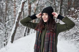 touche le chapeau noir. joyeuse jeune fille dans des vêtements chauds se promener dans la forêt d'hiver pendant la journée photo