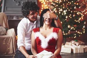 moment que vous avez attendu. femme en robe rouge couvrant ses yeux et recevra un cadeau de noël de son petit ami photo