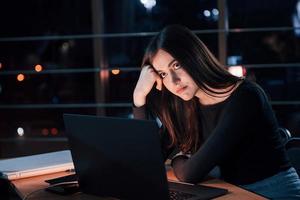 elle ne peut pas rester assise à ne rien faire. jolie femme d'affaires brune travaille seule au bureau la nuit photo