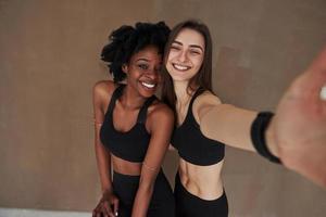 dans une pièce avec un bon éclairage. deux amies multiethniques se tiennent dans le studio avec un fond marron photo