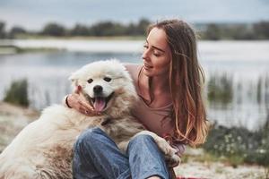 avec la langue tirée. il fait chaud là-bas. fille blonde avec son mignon chien blanc passe un bon moment à passer sur une plage photo