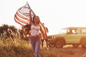 fille court en avant. les amis passent un bon week-end à l'extérieur près de leur voiture verte avec le drapeau américain photo