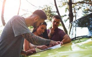 jeunes amis lisant la carte qui se trouve sur le capot d'une jeep verte moderne dans la forêt photo