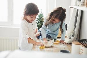 la lumière naturelle du jour par la fenêtre. amis d'âge préscolaire apprenant à cuisiner avec de la farine dans la cuisine blanche photo