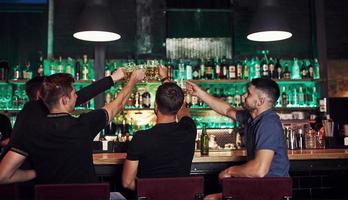 beaucoup de bouteilles d'alcool sur les étagères. amis se reposant dans le pub avec de la bière dans les mains. avoir une conversation photo