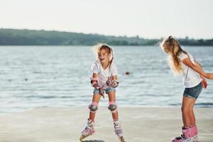 deux enfants apprennent à monter sur des patins à roulettes pendant la journée près du lac photo