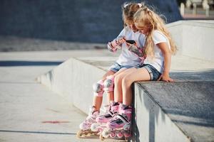 à l'aide d'un téléphone intelligent. sur la rampe pour les sports extrêmes. deux petites filles avec des patins à roulettes à l'extérieur s'amusent photo