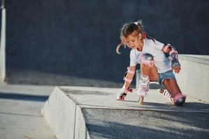 jolie petite fille avec des patins à roulettes à l'extérieur est assise sur la rampe pour les sports extrêmes photo