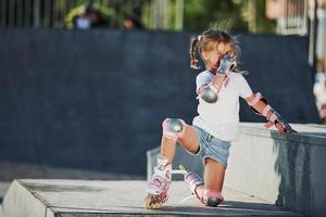 jolie petite fille avec des patins à roulettes à l'extérieur est assise sur la rampe pour les sports extrêmes photo