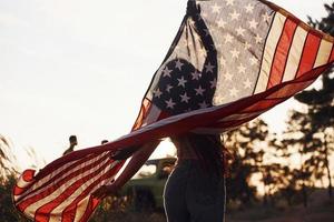 belle lumière. brune avec le drapeau américain dans les mains passe un bon moment et sent la liberté à l'extérieur par temps ensoleillé photo