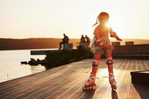 joyeux enfant mignon à cheval sur ses patins à roulettes. lumière du soleil incroyable photo