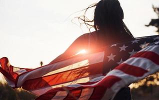 belle lumière. brune avec le drapeau américain dans les mains passe un bon moment et sent la liberté à l'extérieur par temps ensoleillé photo