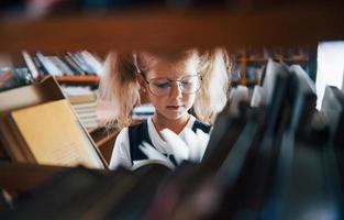 petite fille à lunettes à la recherche d'un livre dans la bibliothèque. conception de l'éducation photo