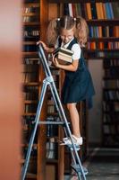 écolière sur l'échelle dans la bibliothèque pleine de livres. conception de l'éducation photo