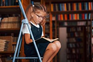 écolière sur l'échelle dans la bibliothèque pleine de livres. conception de l'éducation photo