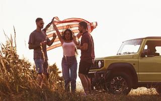 fille avec les mains en l'air. les amis passent un bon week-end à l'extérieur près de leur voiture verte avec le drapeau américain photo