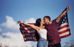 s'embrasser. sent la liberté. beau couple avec drapeau américain passer un bon moment à l'extérieur sur le terrain photo