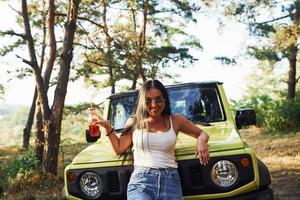 blonde avec de l'alcool à la main se promener dans la forêt contre la jeep verte photo