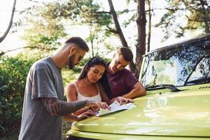 jeunes amis lisant la carte qui se trouve sur le capot d'une jeep verte moderne dans la forêt photo