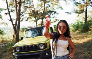 blonde avec de l'alcool à la main se promener dans la forêt contre la jeep verte photo