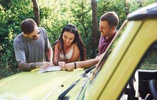 jeunes amis lisant la carte qui se trouve sur le capot d'une jeep verte moderne dans la forêt photo