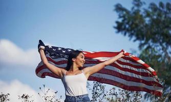 femme patriote court avec le drapeau américain dans les mains à l'extérieur sur le terrain contre le ciel bleu photo