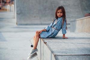petite fille en tenue bleue posant pour un appareil photo dans la ville en s'appuyant sur la rampe