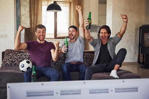 c'est un but. excité trois amis regardant le football à la télévision à la maison ensemble photo