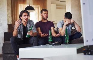 c'est une défaite. tristes trois amis regardant le football à la télévision à la maison ensemble photo