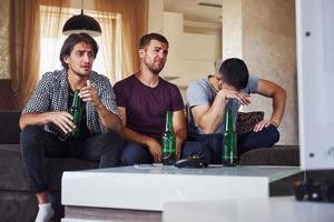 c'est une défaite. tristes trois amis regardant le football à la télévision à la maison ensemble photo