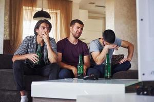 c'est une défaite. tristes trois amis regardant le football à la télévision à la maison ensemble photo