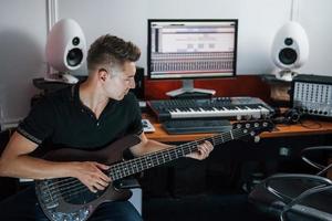 le jeune musicien enregistre la guitare basse à l'intérieur dans le studio photo