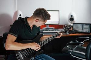 le jeune musicien enregistre la guitare basse à l'intérieur dans le studio photo