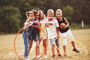 les jeunes enfants avec un ballon de football, un jouet d'avion et des cercles de fitness se tiennent ensemble sur le terrain à la journée ensoleillée photo