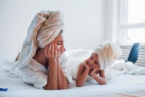 allongé sur un lit blanc ensemble. jeune mère avec sa fille a une journée de beauté à l'intérieur dans la chambre photo