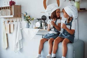 assis sur le frigo. les enfants de la famille en uniforme de chef blanc mangent de la nourriture dans la cuisine
