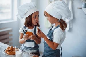 les enfants de la famille en uniforme de chef blanc mangent de la nourriture dans la cuisine photo