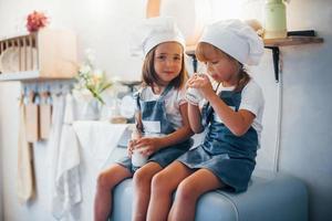 assis sur le frigo. les enfants de la famille en uniforme de chef blanc mangent de la nourriture dans la cuisine