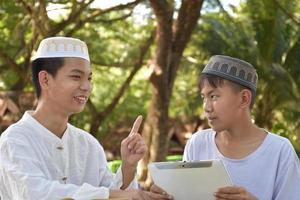 les garçons musulmans asiatiques s'assoient ensemble dans le parc de l'école pour lire et apprendre leur activité quotidienne et faire leurs devoirs pendant leurs temps libres avant de rentrer à la maison, mise au point douce et sélective. photo