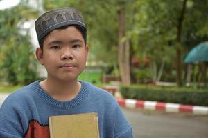 portrait asiatique garçon musulman ou islamique assis dans le parc de l'école et souriant joyeusement, mise au point douce et sélective. photo