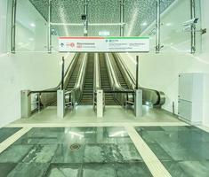 à l'intérieur de la gare, de hauts escalators sont installés pour monter vers d'autres lignes de métro. voyager en transports en commun. au-dessus des escalators il y a des panneaux avec les noms des stations photo