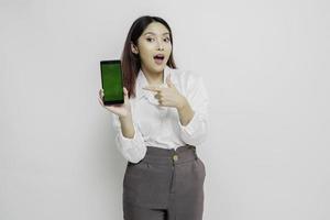 femme asiatique surprise portant une chemise blanche montrant l'espace de copie sur son smartphone, isolée par fond blanc photo