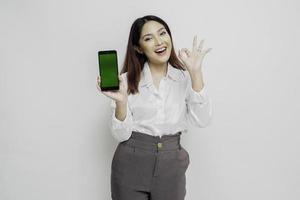 un portrait d'une femme asiatique excitée portant une chemise blanche tout en tenant son téléphone et en gesticulant signe d'approbation, isolée sur fond blanc photo